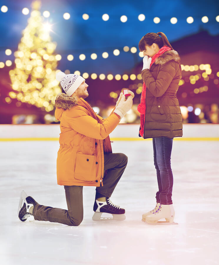 A man proposing to a woman on one knee while ice skating on an ice rink