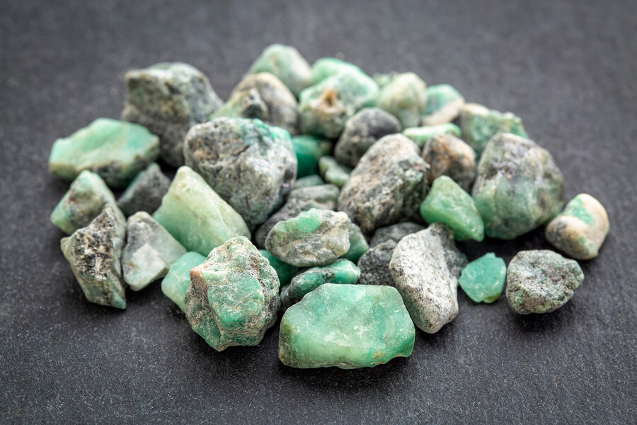 a pile of raw emerald gemstones on a grey slate