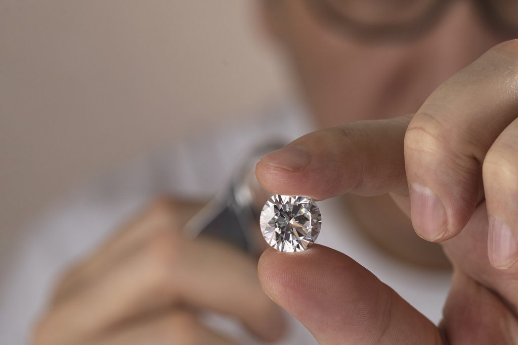 A jeweller looking at a diamond in his hand with a magnifying glass