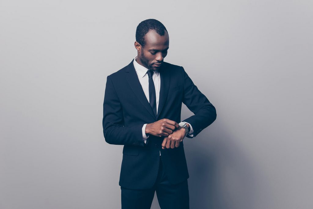 A smart Black man wearing a suit and looking at his wristwatch