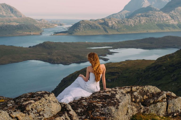 A Norwegian bride wearing a white wedding dress sat looking over the Norwegian fjords in Norway. Norwegian wedding traditions