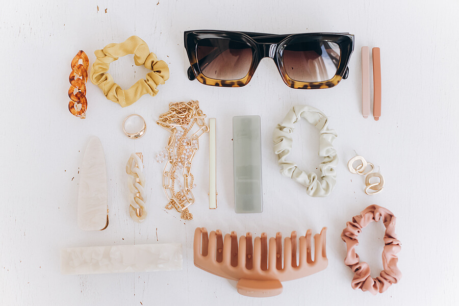 How to travel with jewellery. Modern summer accessories layout. Golden jewellery, sunglasses, hair clips and hairbands, barrettes on white table top view. Feminine essentials. Boho colorful accessories